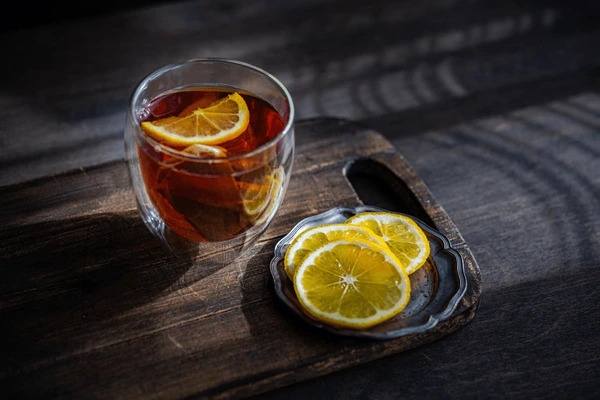 Glass cup of black tea infused with fresh lemon slices, served on a wooden board for a refreshing and antioxidant-rich tea experience