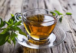 Cup of green tea served in a glass teacup with fresh green tea leaves on a wooden surface.