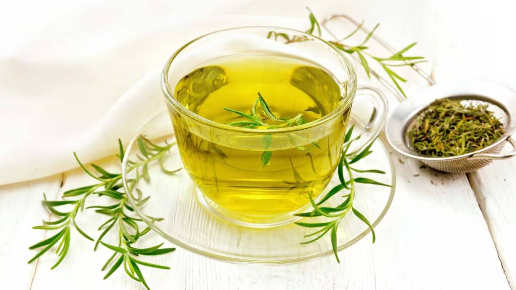 Glass cup of freshly brewed rosemary tea with rosemary sprigs on a white wooden table, showcasing herbal tea benefits and natural wellness ingredients.