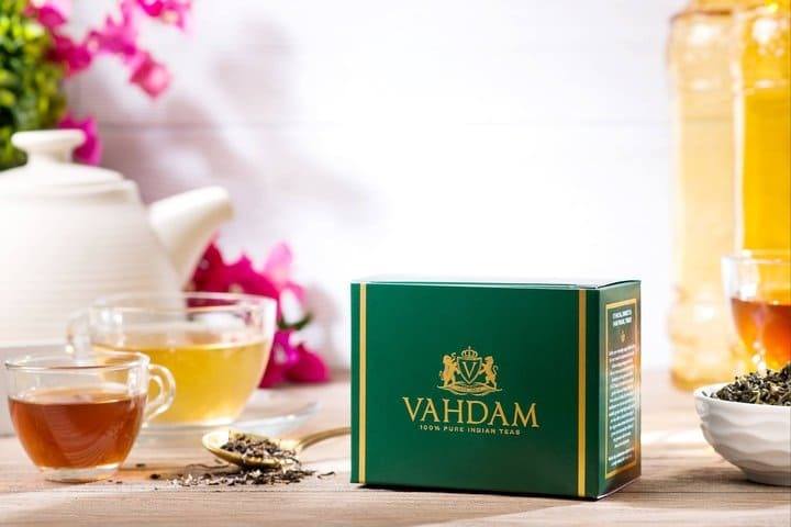 Vahdam premium Indian tea box displayed with brewed tea cups and loose leaf tea on a bright wooden background.