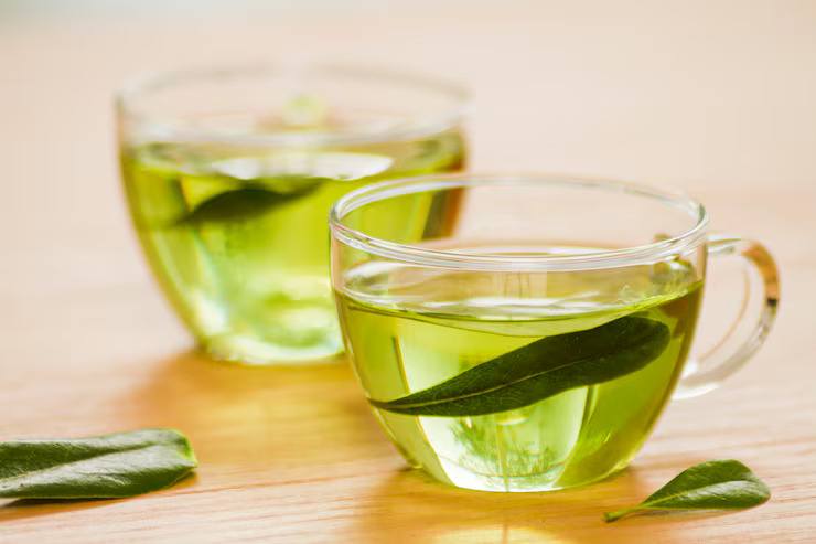 Clear glass cups of freshly brewed green tea with tea leaves on a wooden surface, showcasing antioxidant-rich green tea known for its health benefits and refreshing taste.