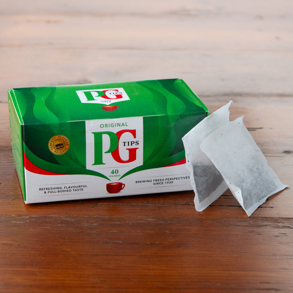 PG Tips Original black tea box with pyramid tea bags displayed on a wooden table.