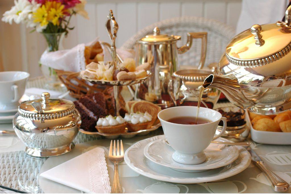 Classic British afternoon tea setting with fine china, silver teapots, pastries, cakes, and a cup of freshly poured black tea.